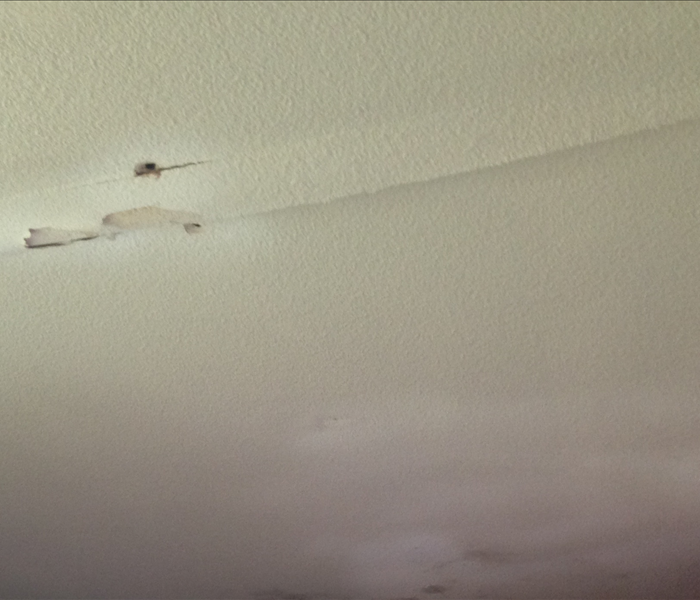 White ceiling with small holes and paint separating from the drywall due to a broken pipe