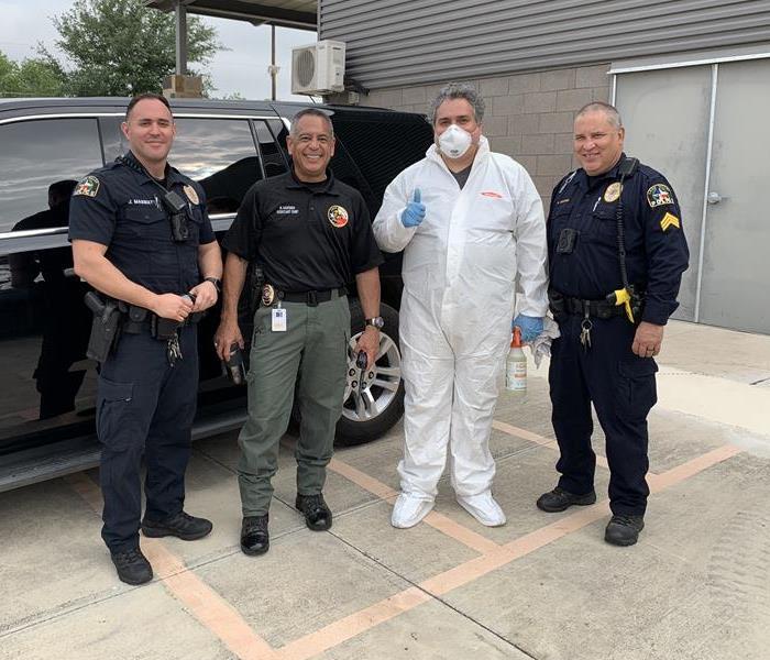 Three Leon Valley police officers and one SERVPRO® of Braun Station technician in coveralls stand in front of an unmarked SUV
