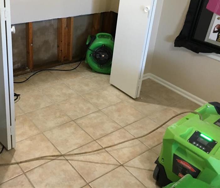 One air mover, green, in a closet with walls flood cut, and a green dehumidifier on tile flooring