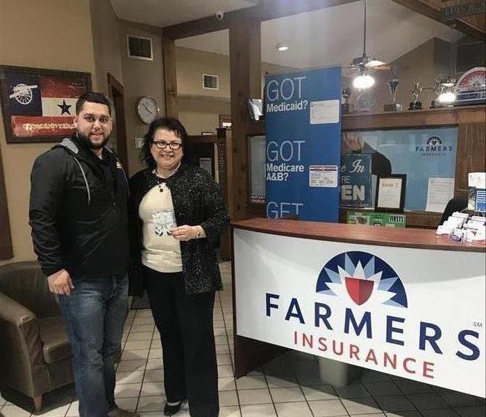 One man and one woman standing next to a Farmers Insurance sign