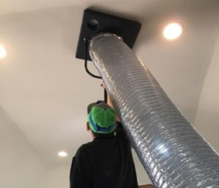 Men in green baseball hat, next to silver duct work