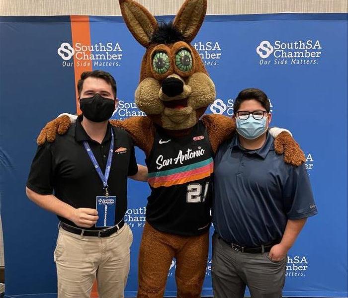 Two marketers from SERVPRO posing with the Spurs Coyote in front of a South San Antonio Chamber of Commerce backdrop