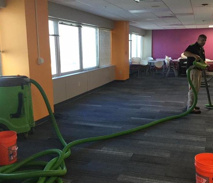 Man using green extractor to extract water from a commercial office's carpet