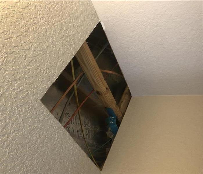 Hole in ceiling showing exposed wood framework after a water damage