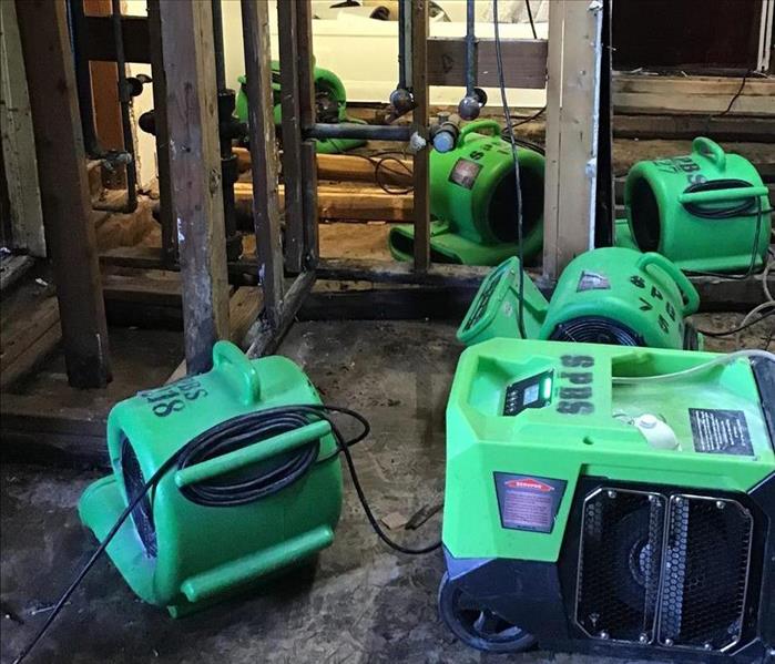 Professional SERVPRO green air movers and dehumidifiers are placed in dining room with no floor and torn out drywall