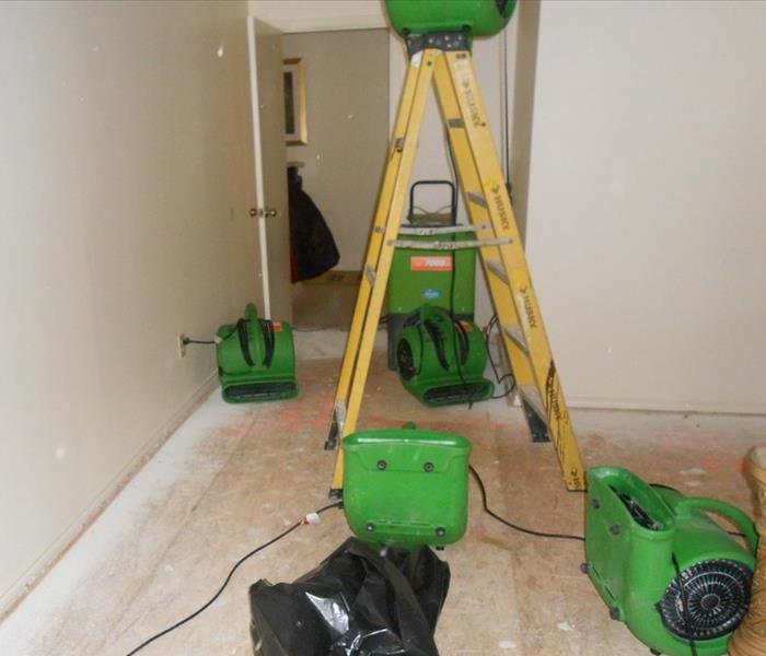 Four green air movers, a yellow ladder, and a green dehumidifier in a room